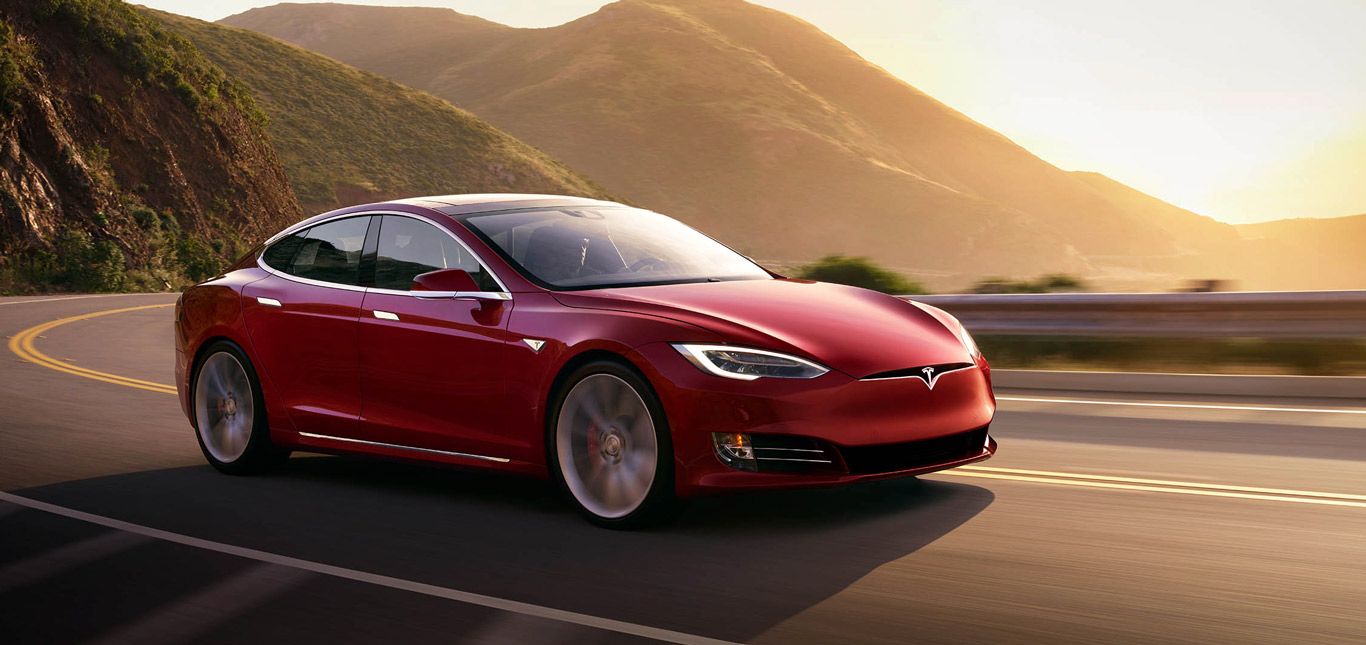 Ein roter Tesla Model S auf einer Landstraße.