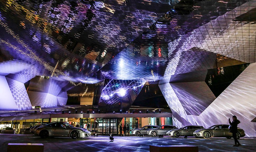 Nachtaufnahme mehrerer grauer Porsches vor bunt leuchtender kubistischer Architektur