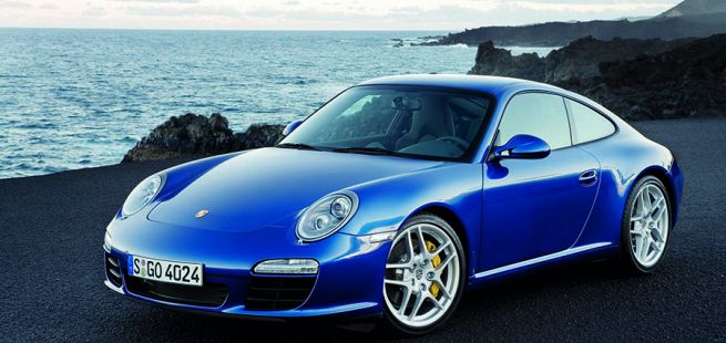 Blauer Porsche 911 997 von schräg links vorne am Meer stehend